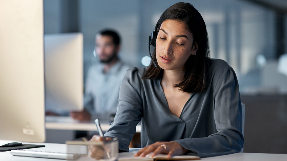decorative image of a woman at a computer wearing a headset and holding a pen